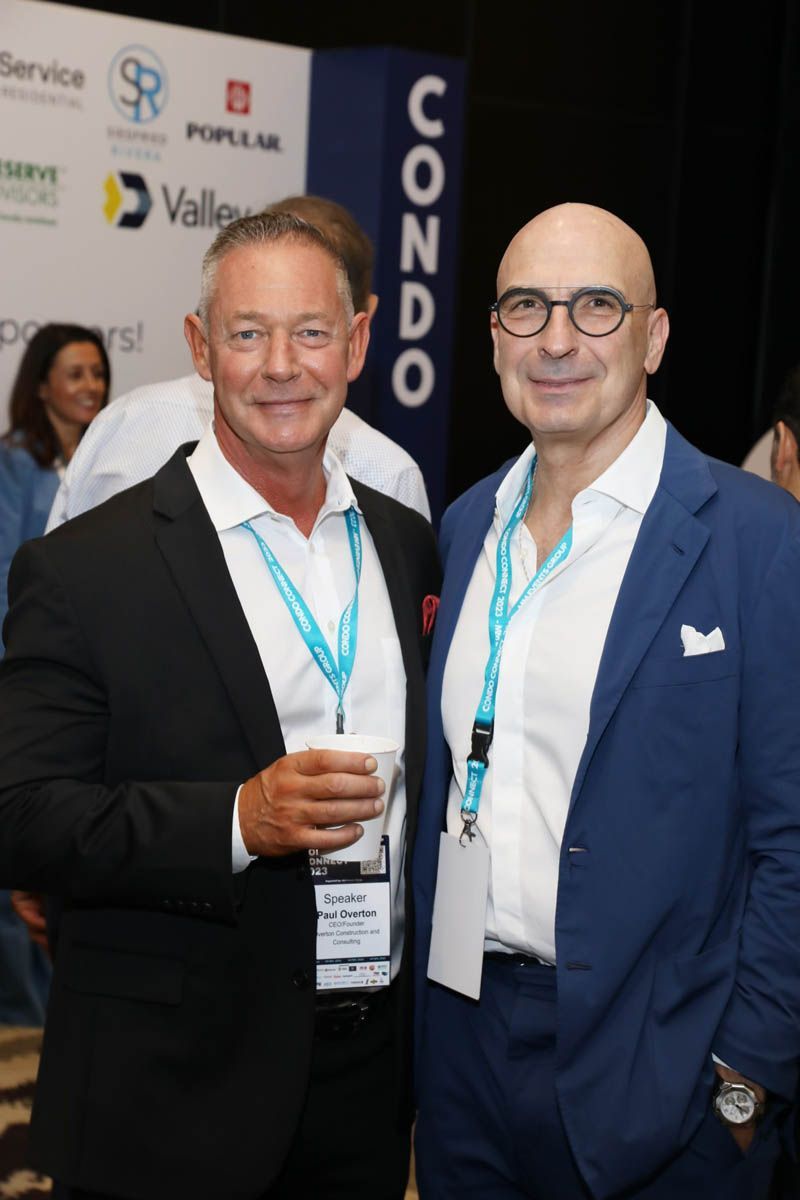 Two men are posing for a picture in front of a banner that says condo