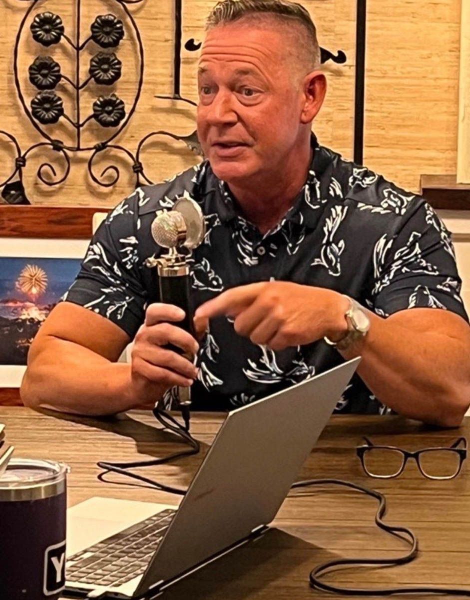 A man is sitting at a table with a laptop and a microphone.