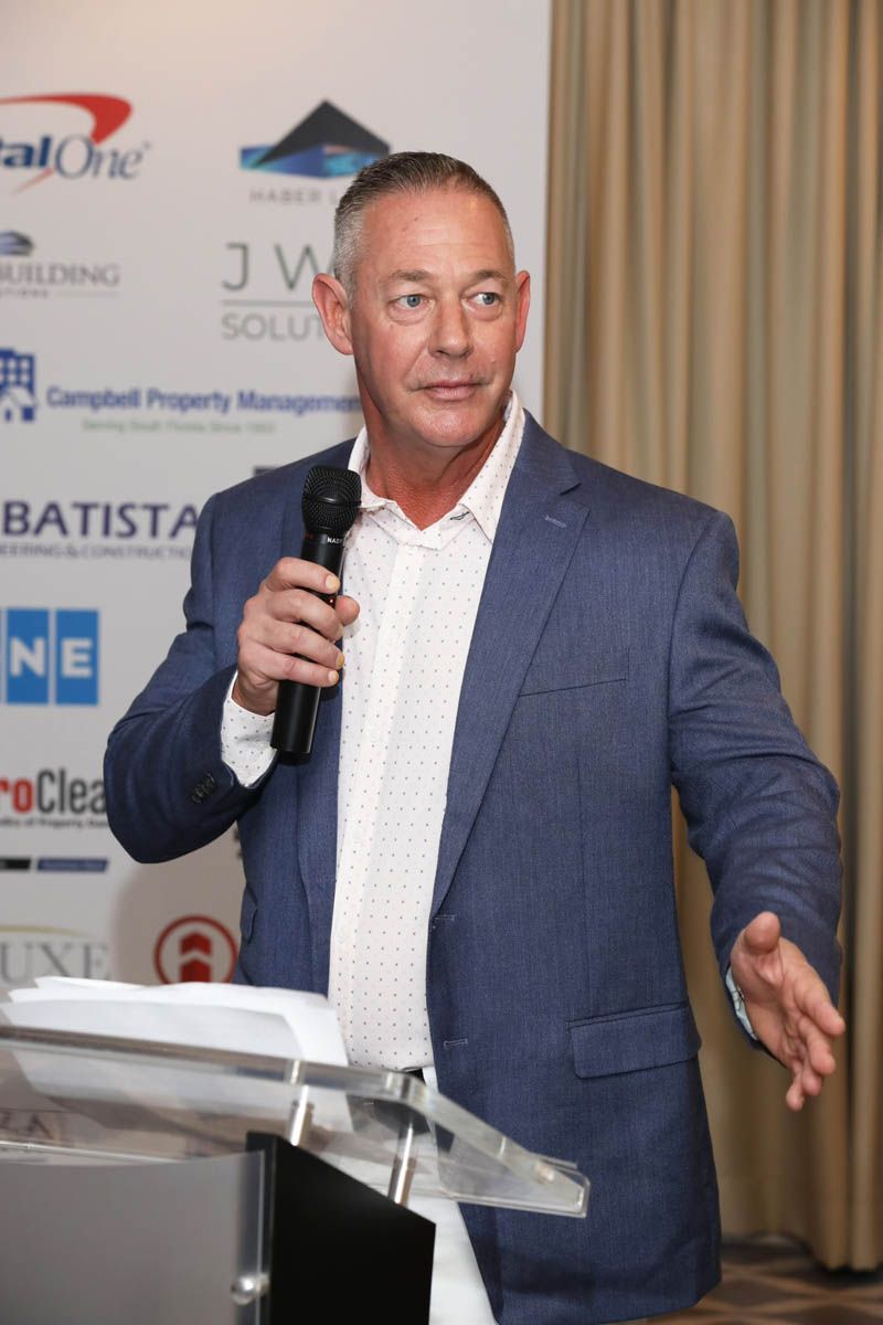 A man in a suit is standing at a podium holding a microphone.