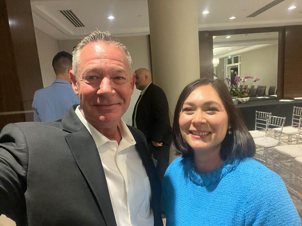 A man in a suit and a woman in a blue sweater are posing for a picture.