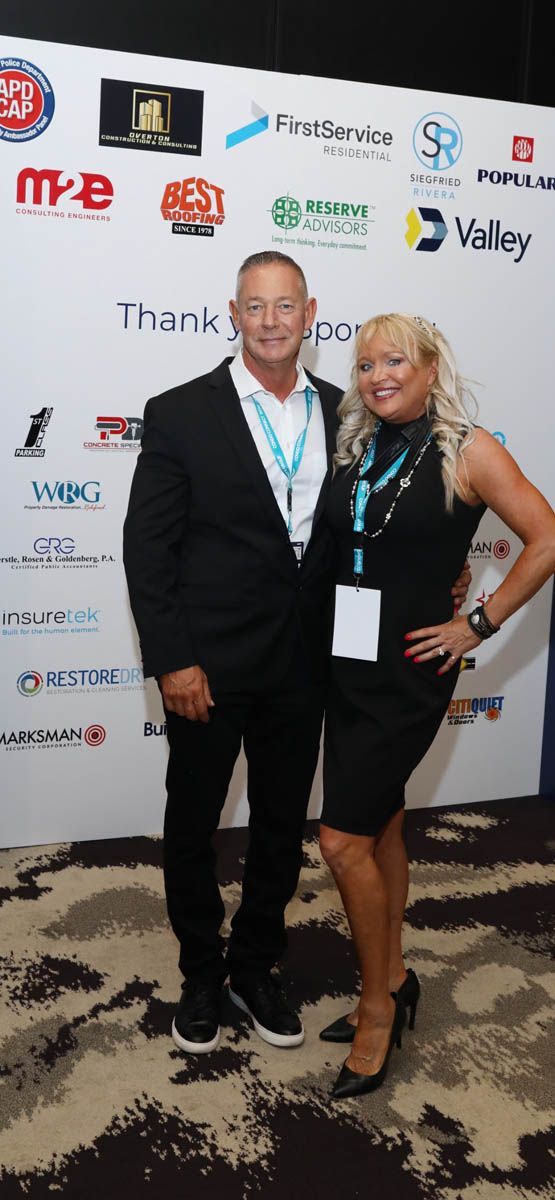 A man and a woman are posing for a picture in front of a wall with logos on it.