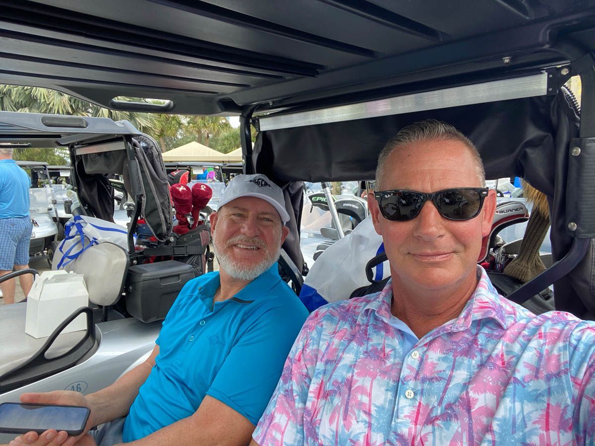 Two men are sitting in a golf cart taking a selfie.