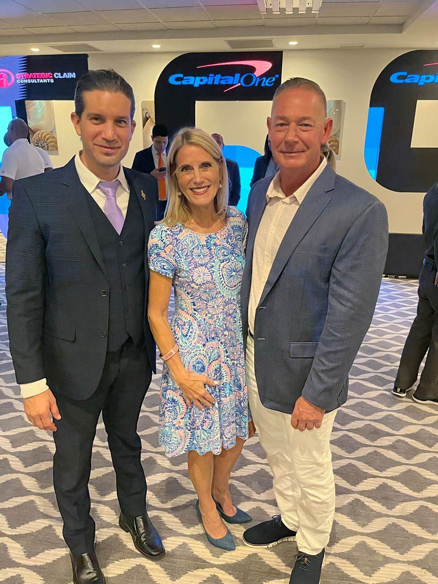 Three people are posing for a picture in a room with a capital one sign in the background.