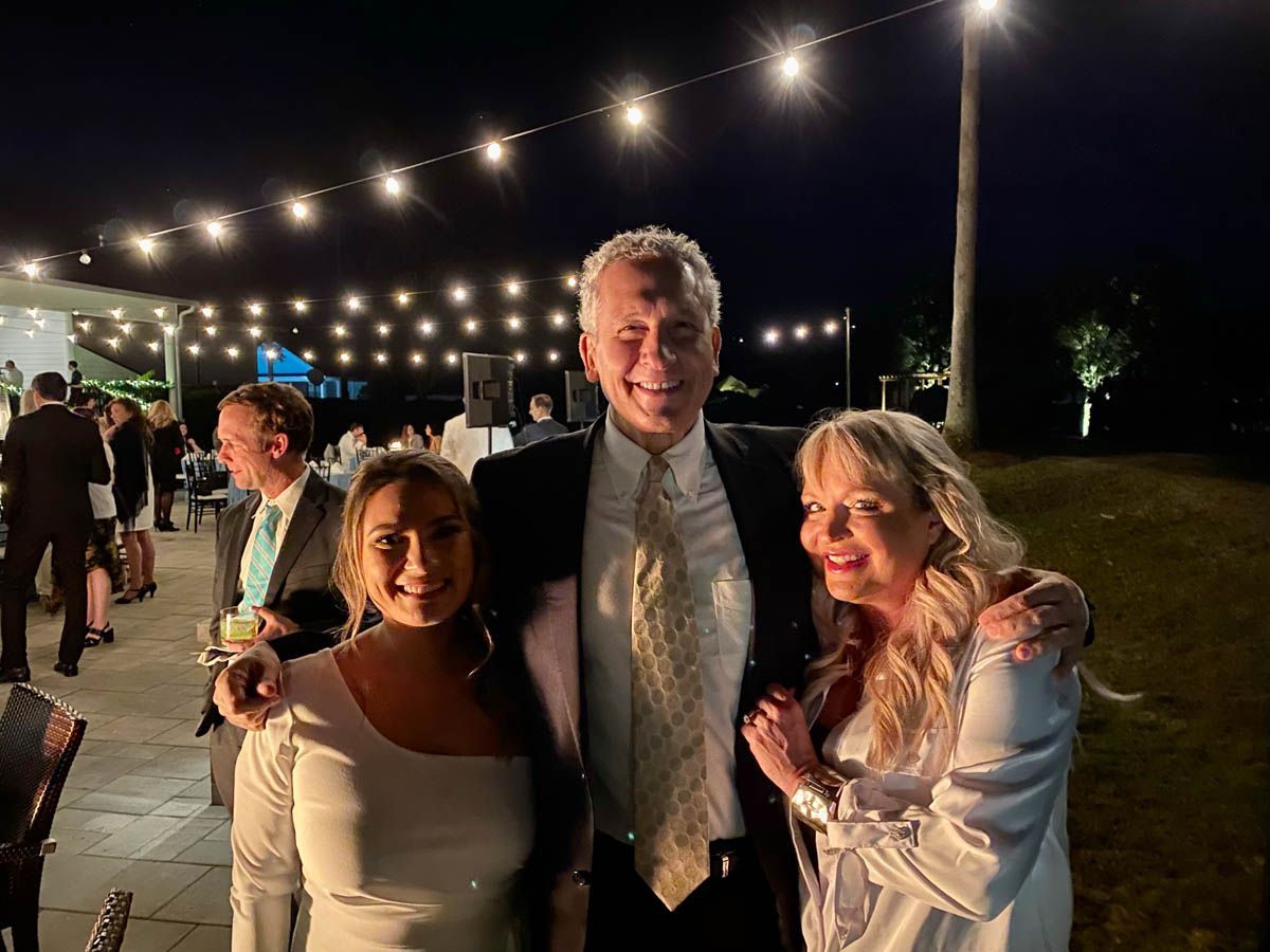 A man and two women are posing for a picture at a wedding reception.