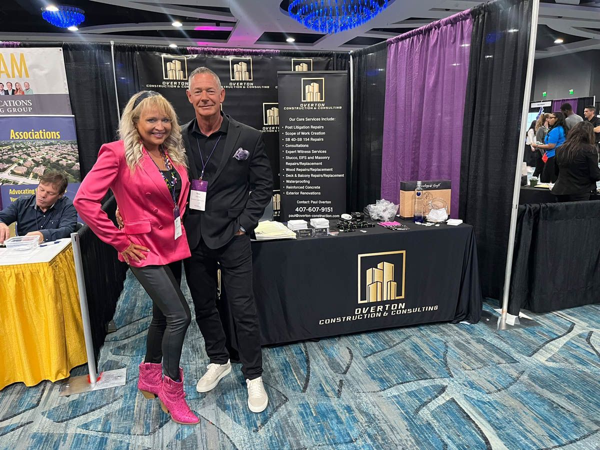 A man and a woman are standing in front of a booth at a convention.