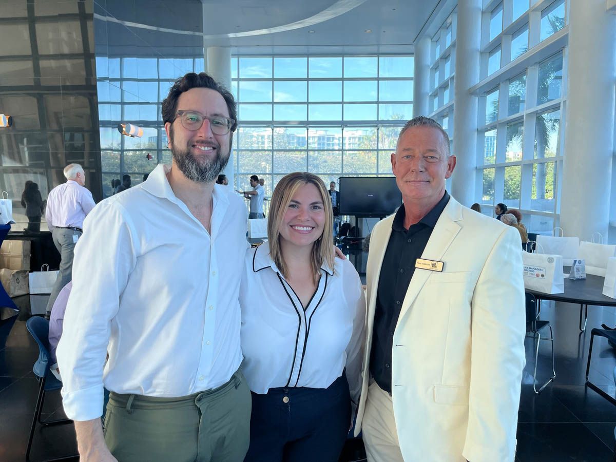 Three people are posing for a picture in a room with a lot of windows.