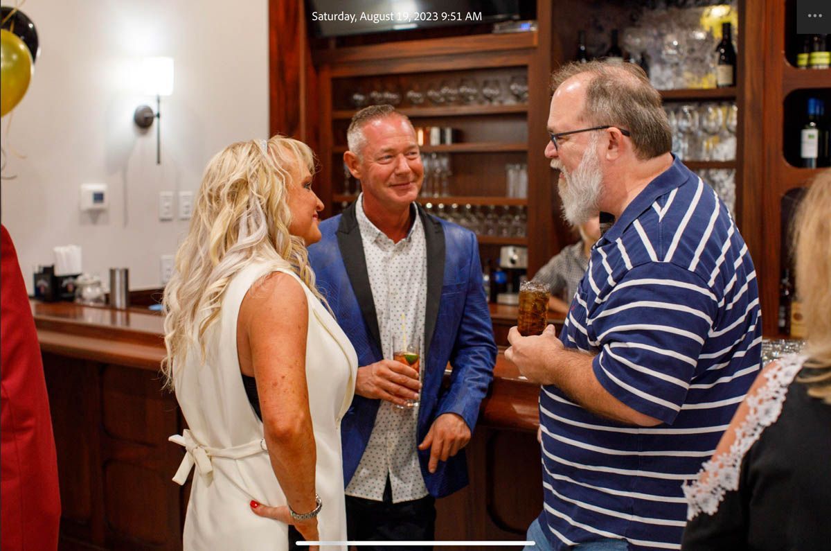 A group of people are standing around a bar talking to each other.