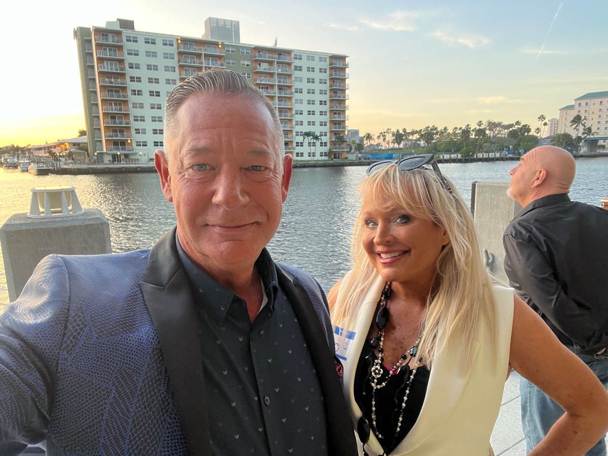 A man and a woman are posing for a picture in front of a body of water.