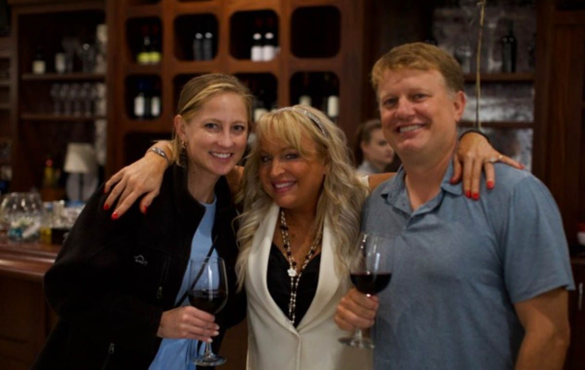 A man and two women are posing for a picture while holding wine glasses.