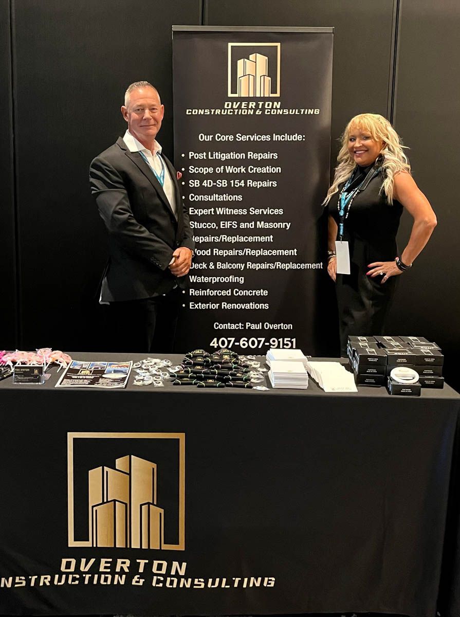 A man and a woman are shaking hands in front of a sign for overton construction & consulting