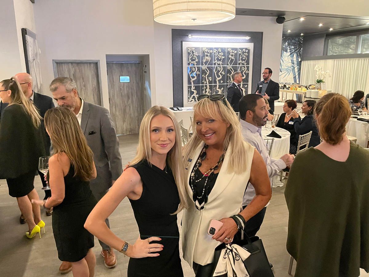 Two women are posing for a picture in a room with other people.