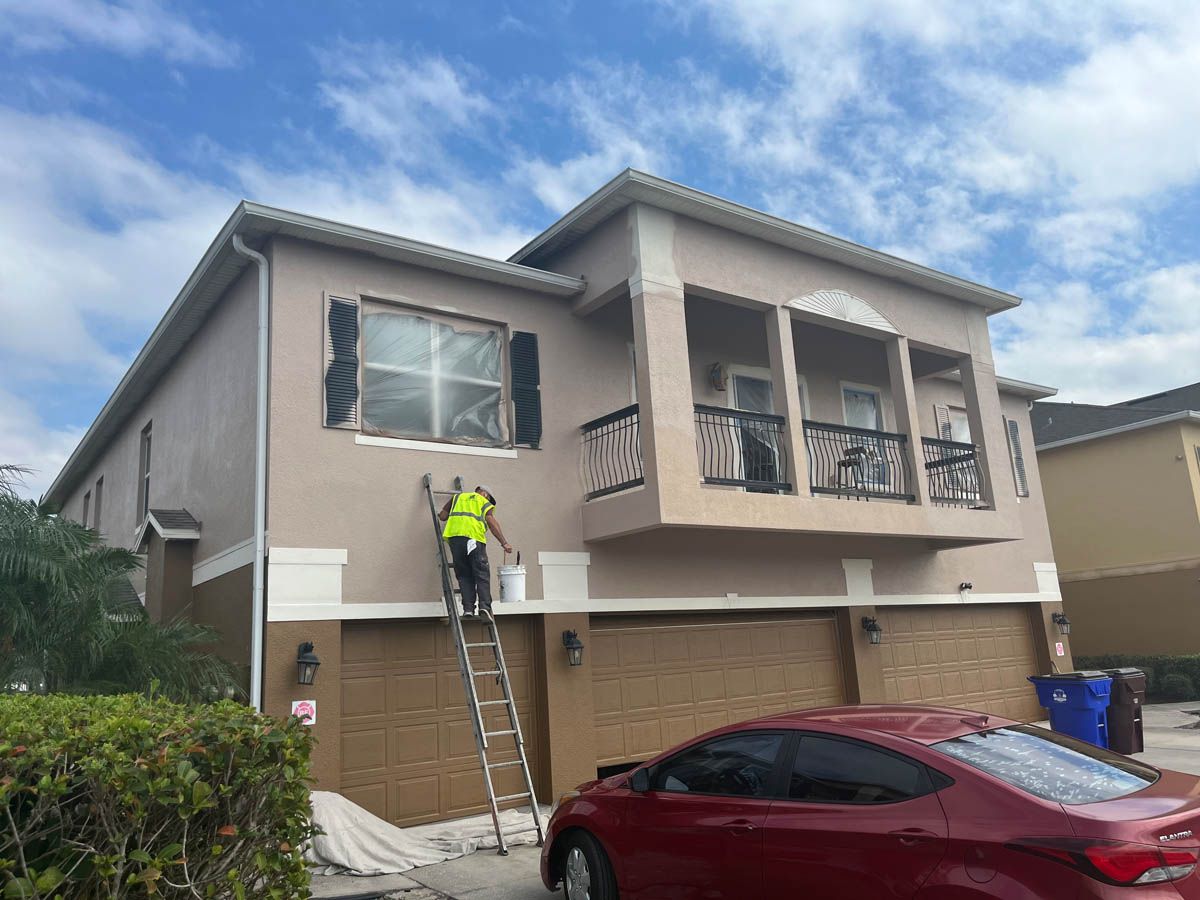 A man is standing on a ladder painting the side of a house.