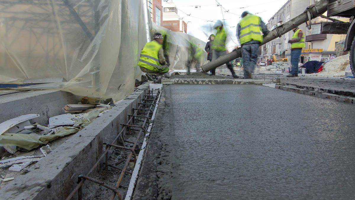 A group of construction workers are pouring concrete on a sidewalk.