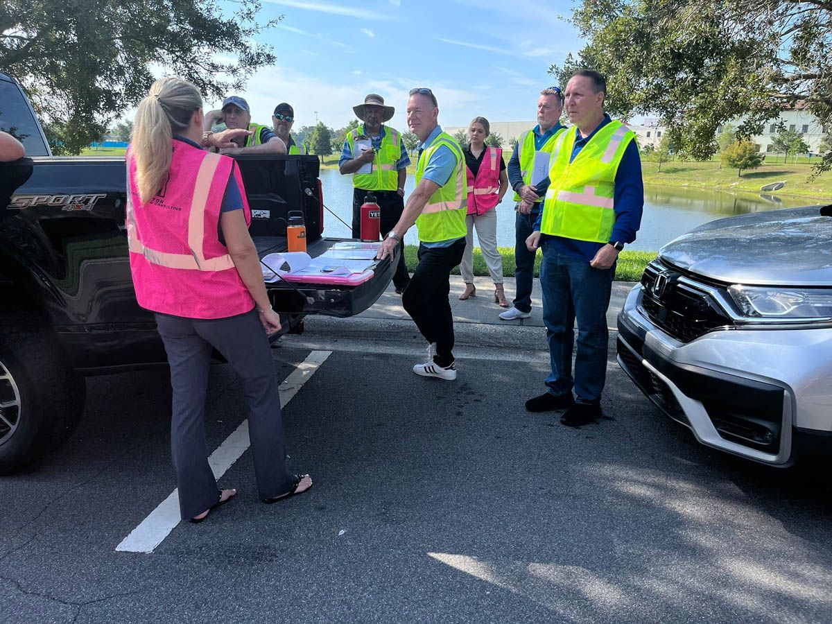 A group of people in safety vests are standing in a parking lot.