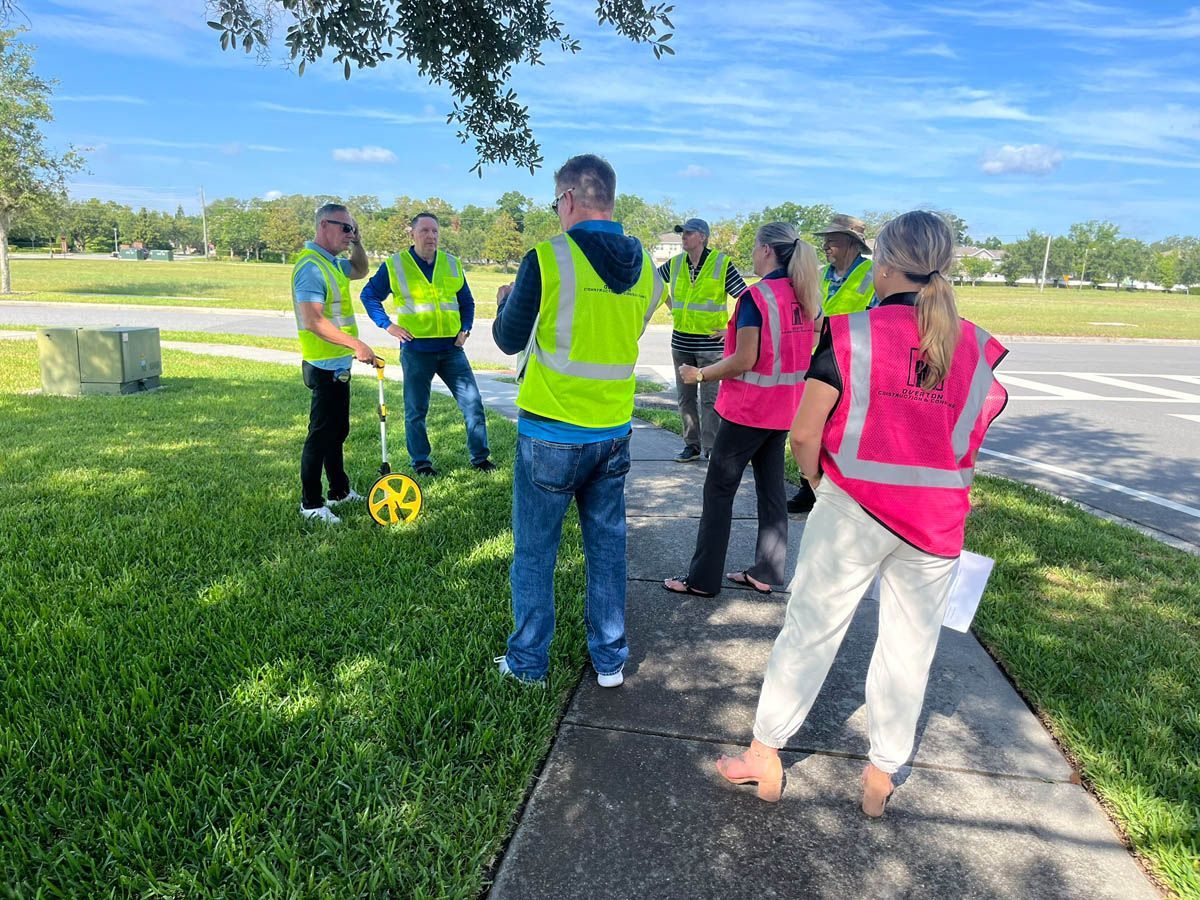 A group of people in safety vests are standing on a sidewalk.