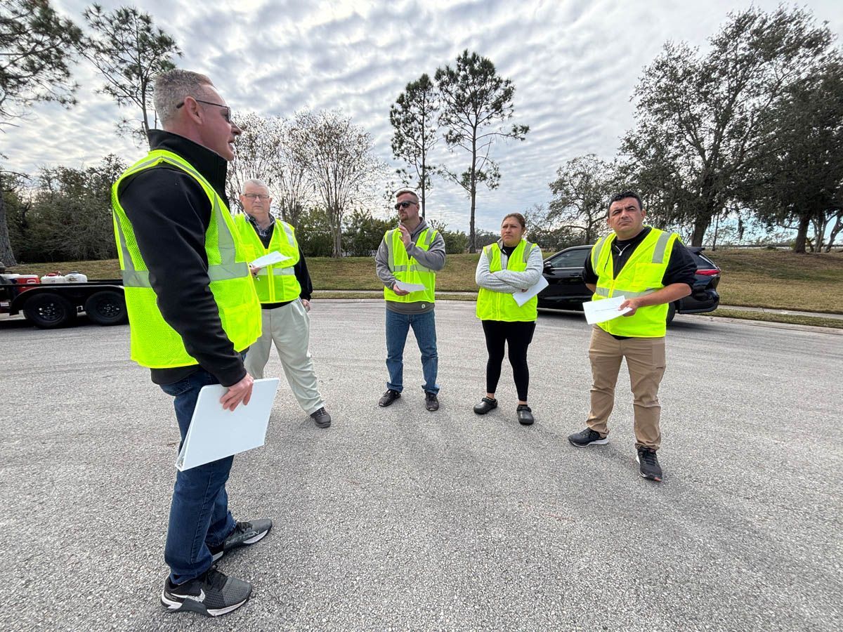 A group of people wearing safety vests are standing in a parking lot.