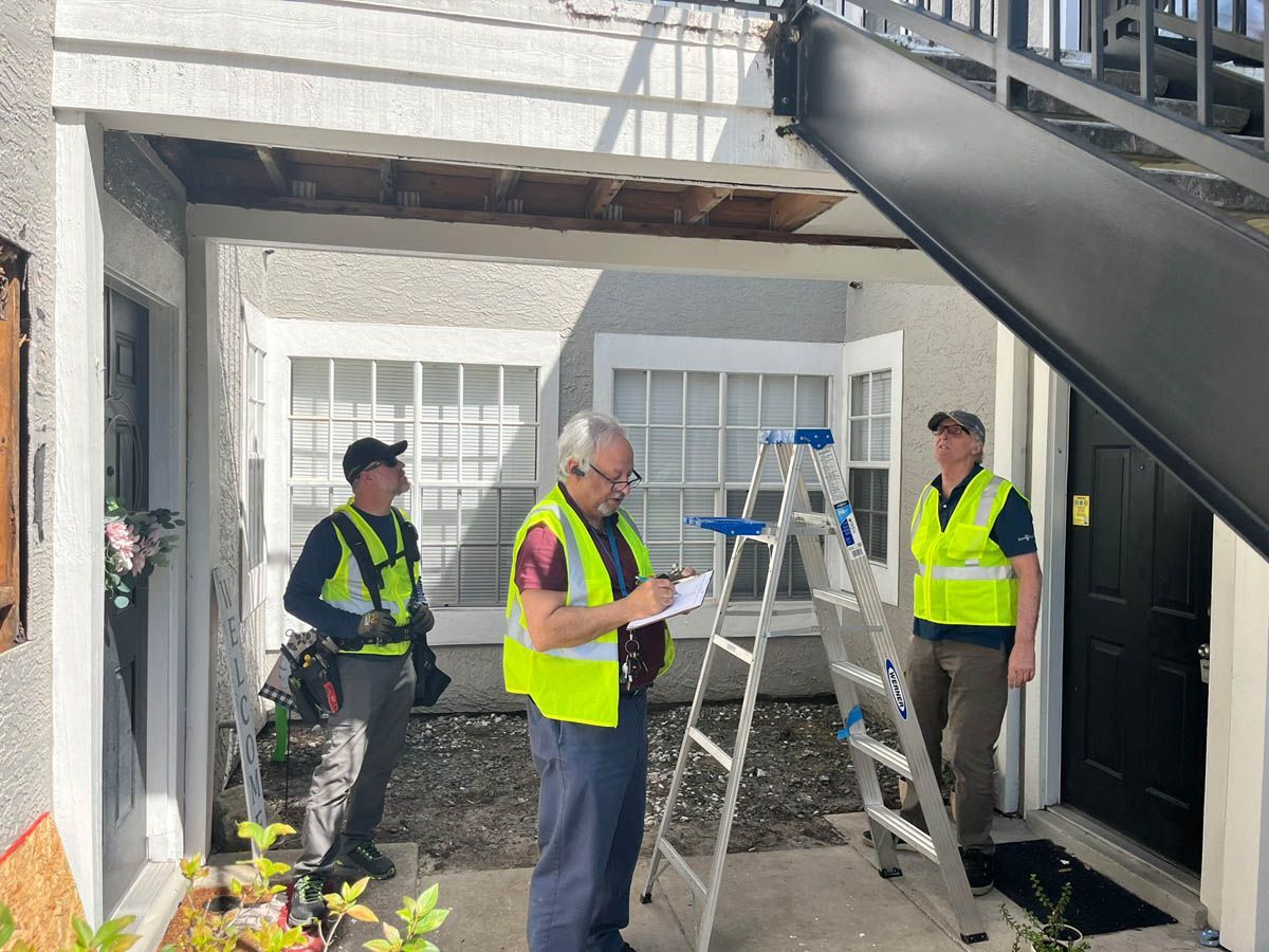 Two men in yellow vests are standing next to a ladder in front of a building.