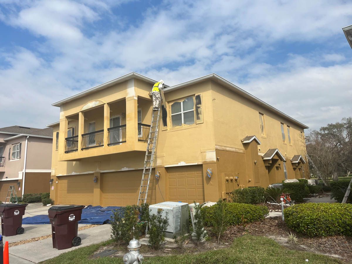 A man is standing on a ladder painting the side of a house.