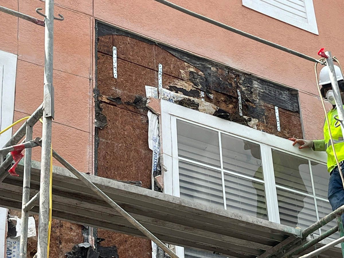 A man is standing on a scaffolding holding a window frame.