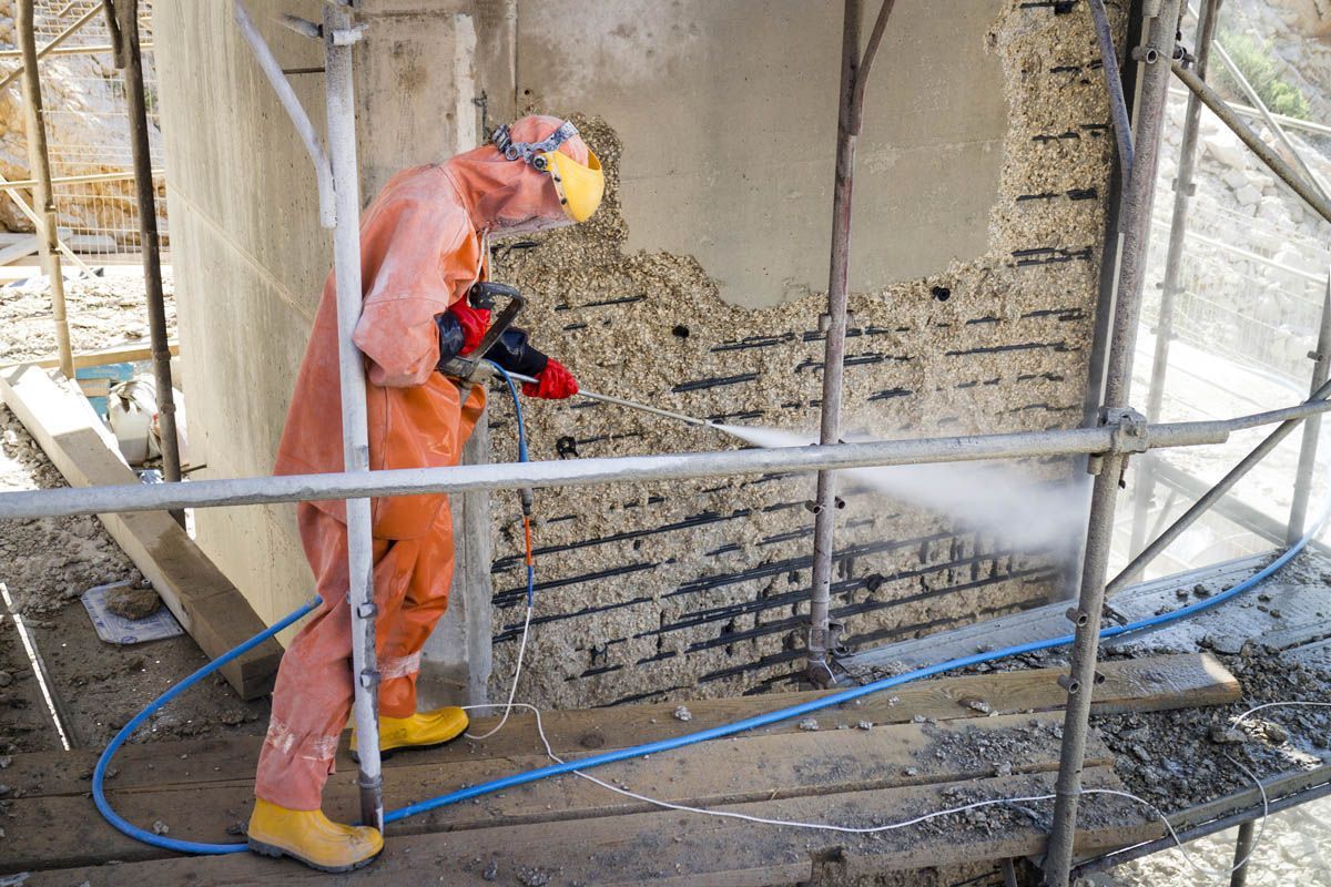 A man in a protective suit is spraying a wall with a high pressure washer.