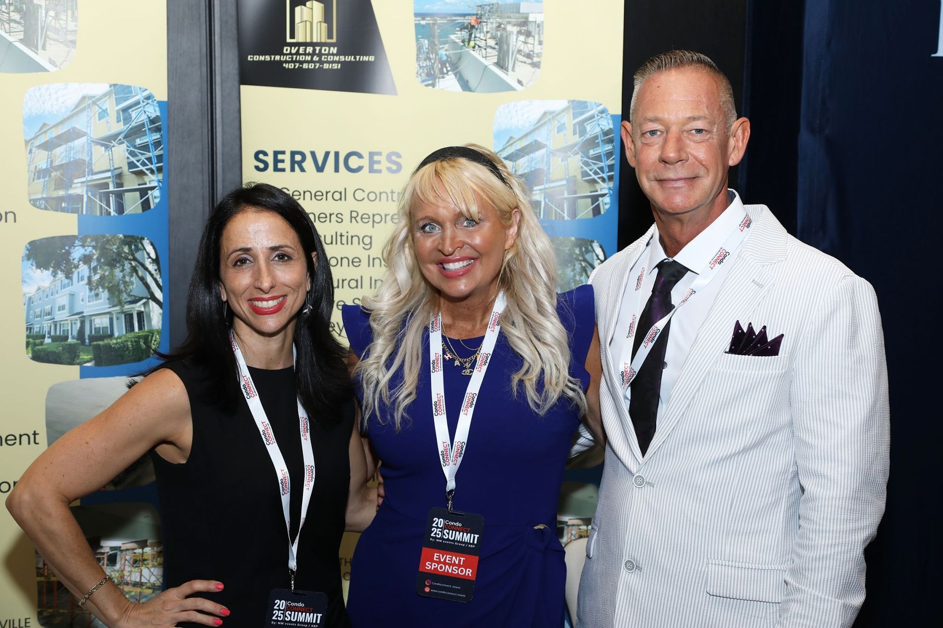 Three people smiling at a business conference booth; two women and a man.
