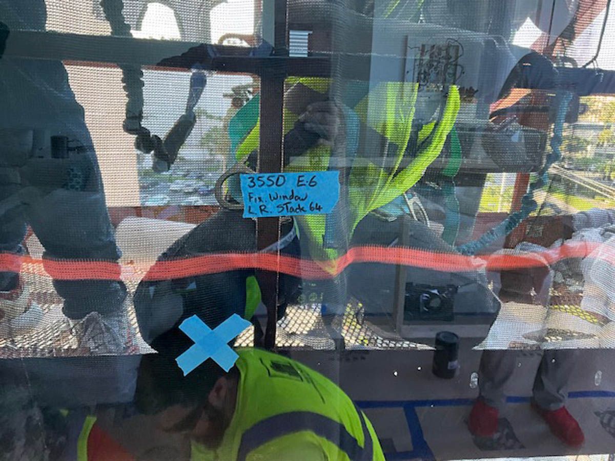 A man in a yellow safety vest is working on a glass window.