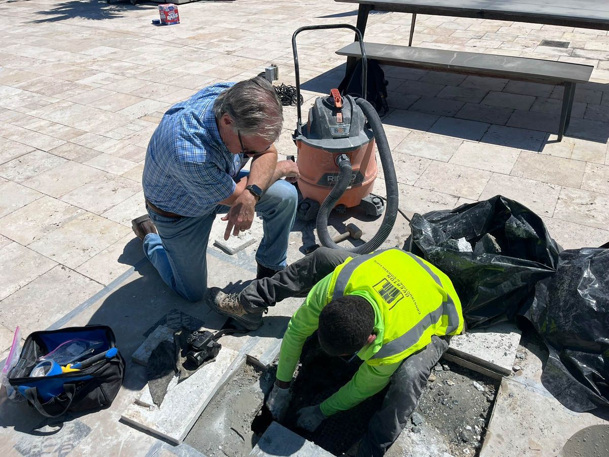 Two men are working on a hole in the ground with a vacuum cleaner.