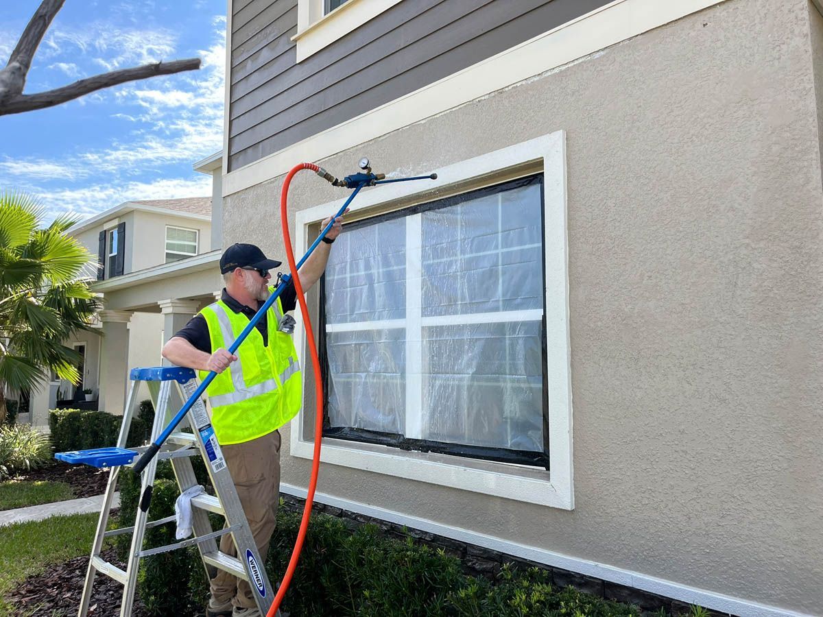 A man is standing on a ladder cleaning a window with a hose.