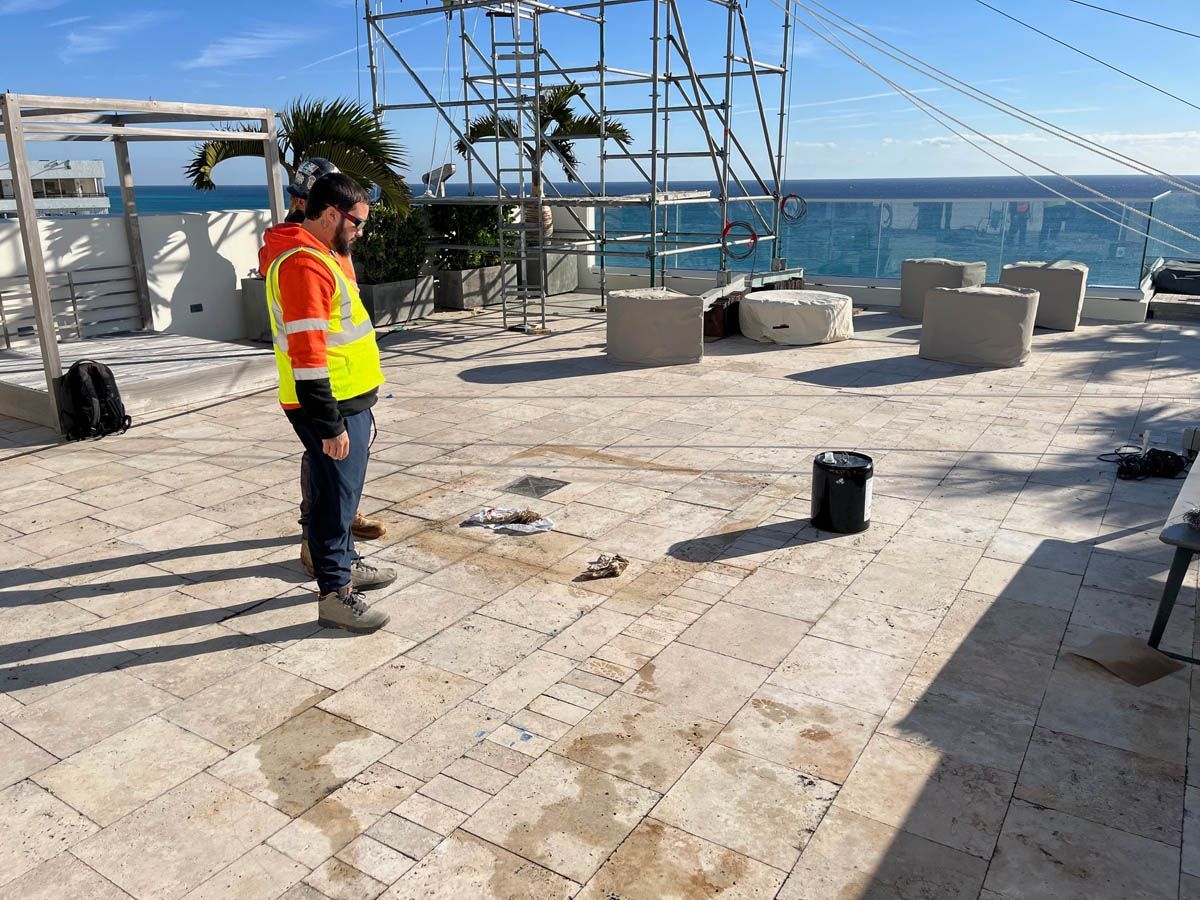 A man in a yellow vest is standing on a roof overlooking the ocean.