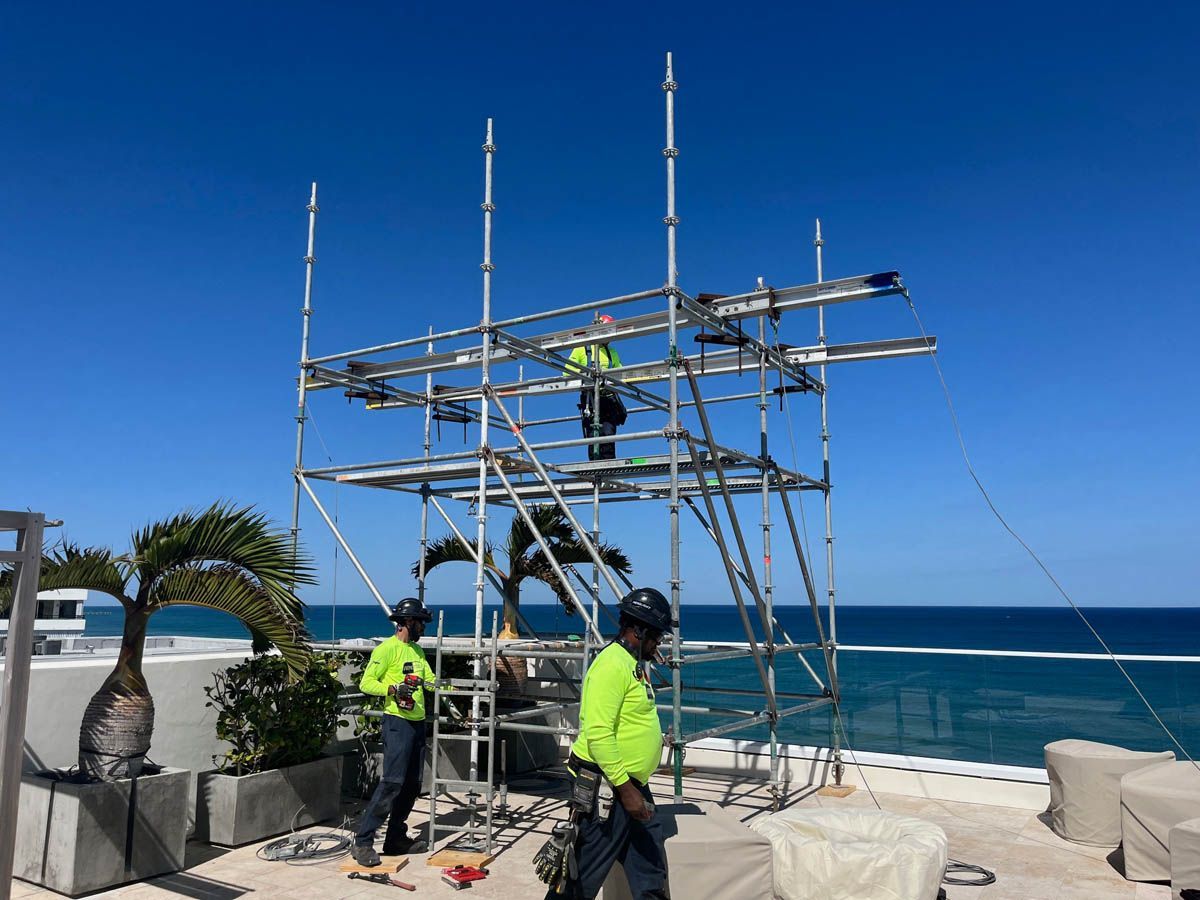 A group of construction workers are working on scaffolding on a balcony overlooking the ocean.