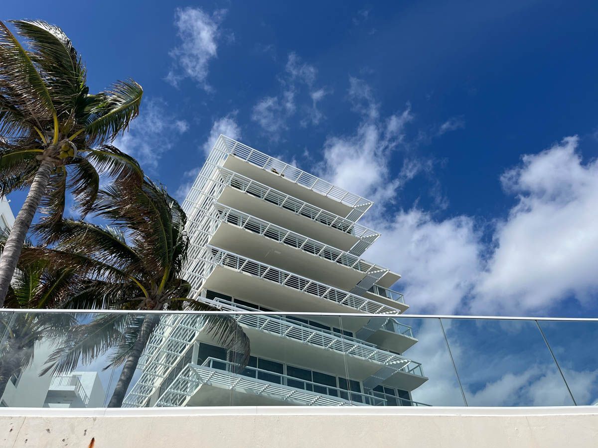A tall building with a glass railing and palm trees in front of it.