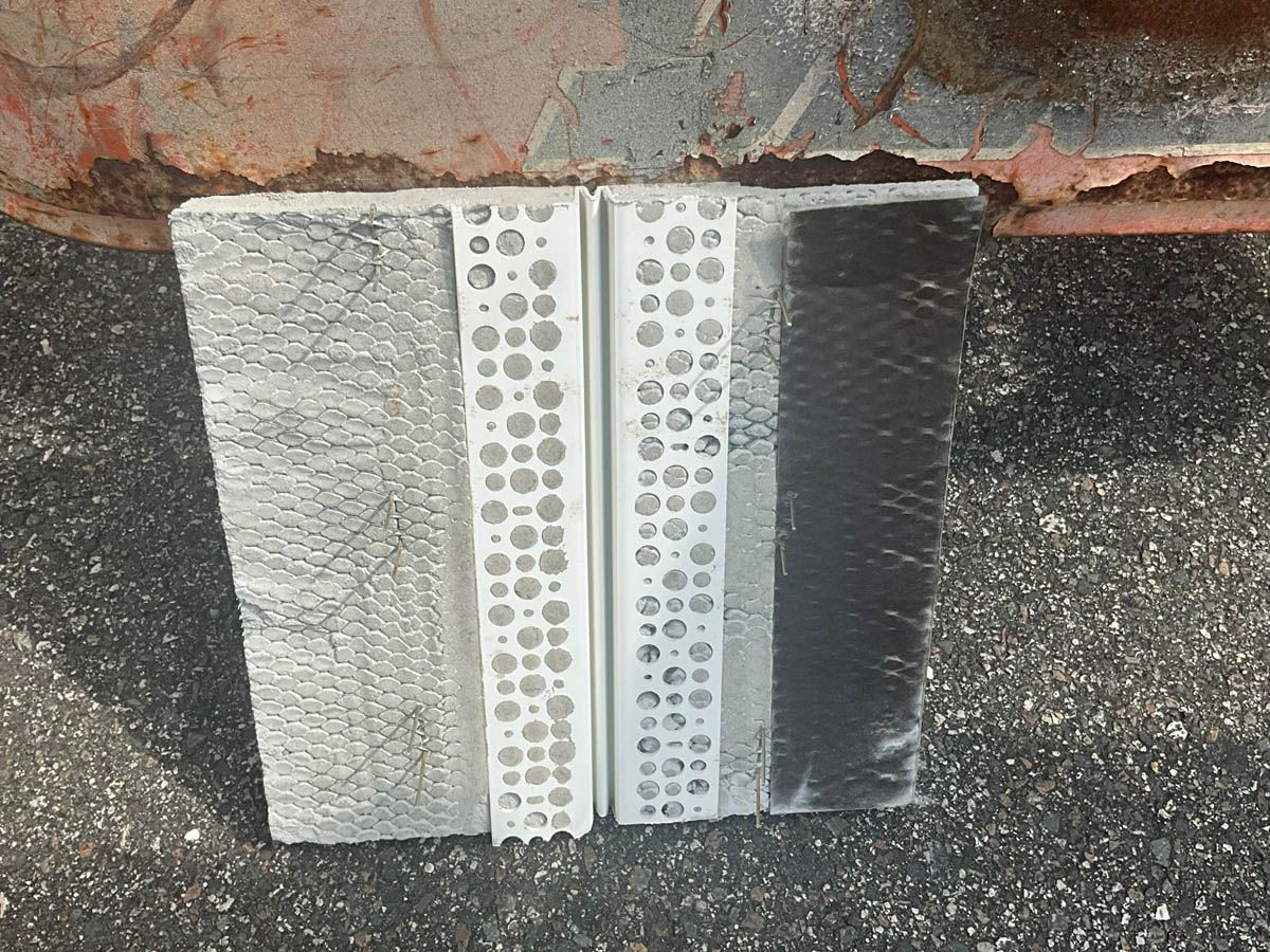 A piece of metal with holes in it is sitting on the ground next to a brick wall.