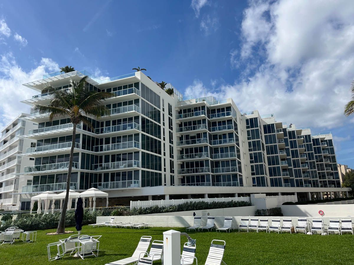 A large building with a lot of windows is surrounded by lawn chairs and umbrellas.