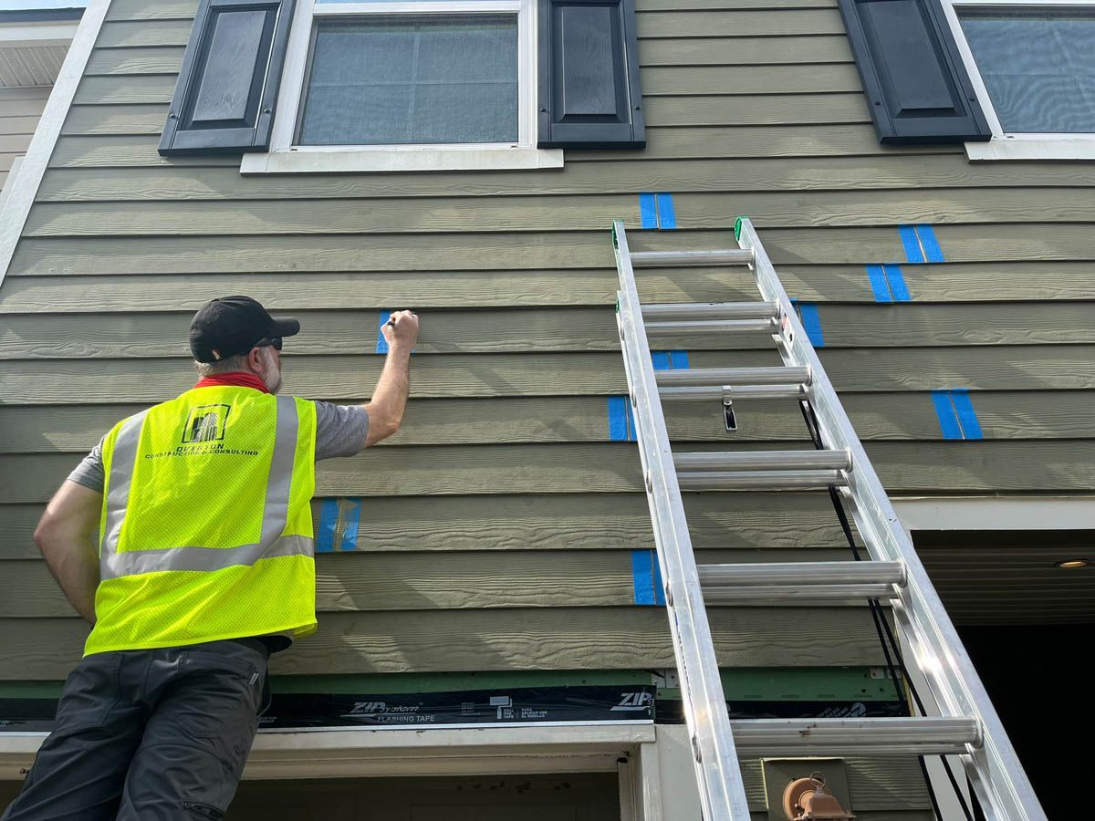 A man is standing on a ladder painting the side of a house.