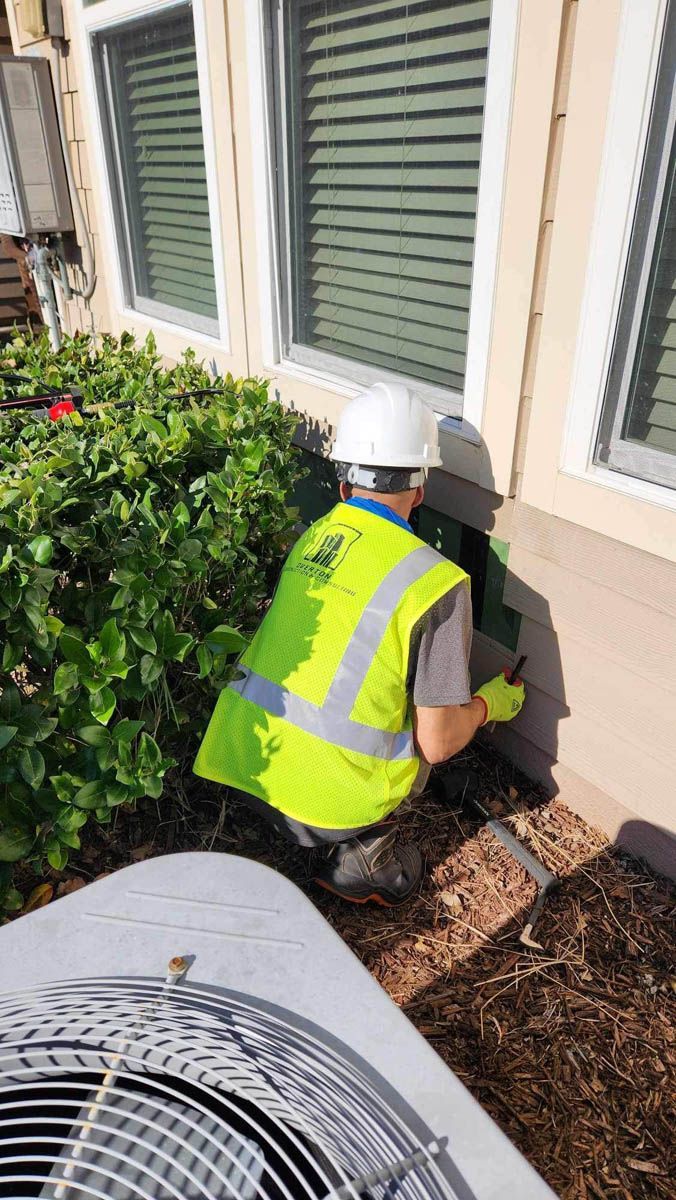 A man in a yellow vest and hard hat is kneeling in front of a house.