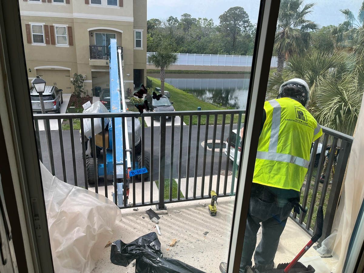 A man in a yellow vest is working on a balcony.