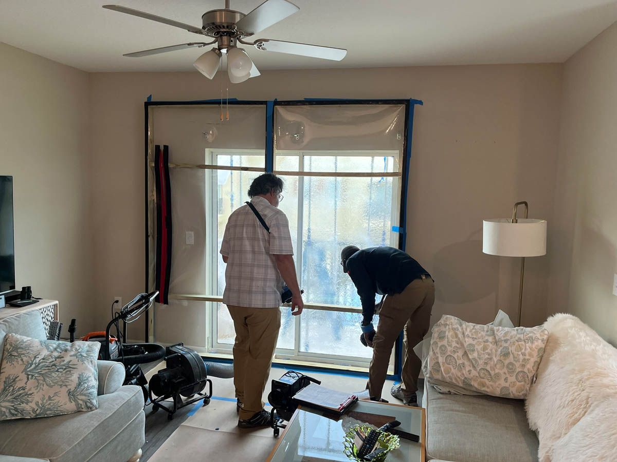 Two men are working on a sliding glass door in a living room.