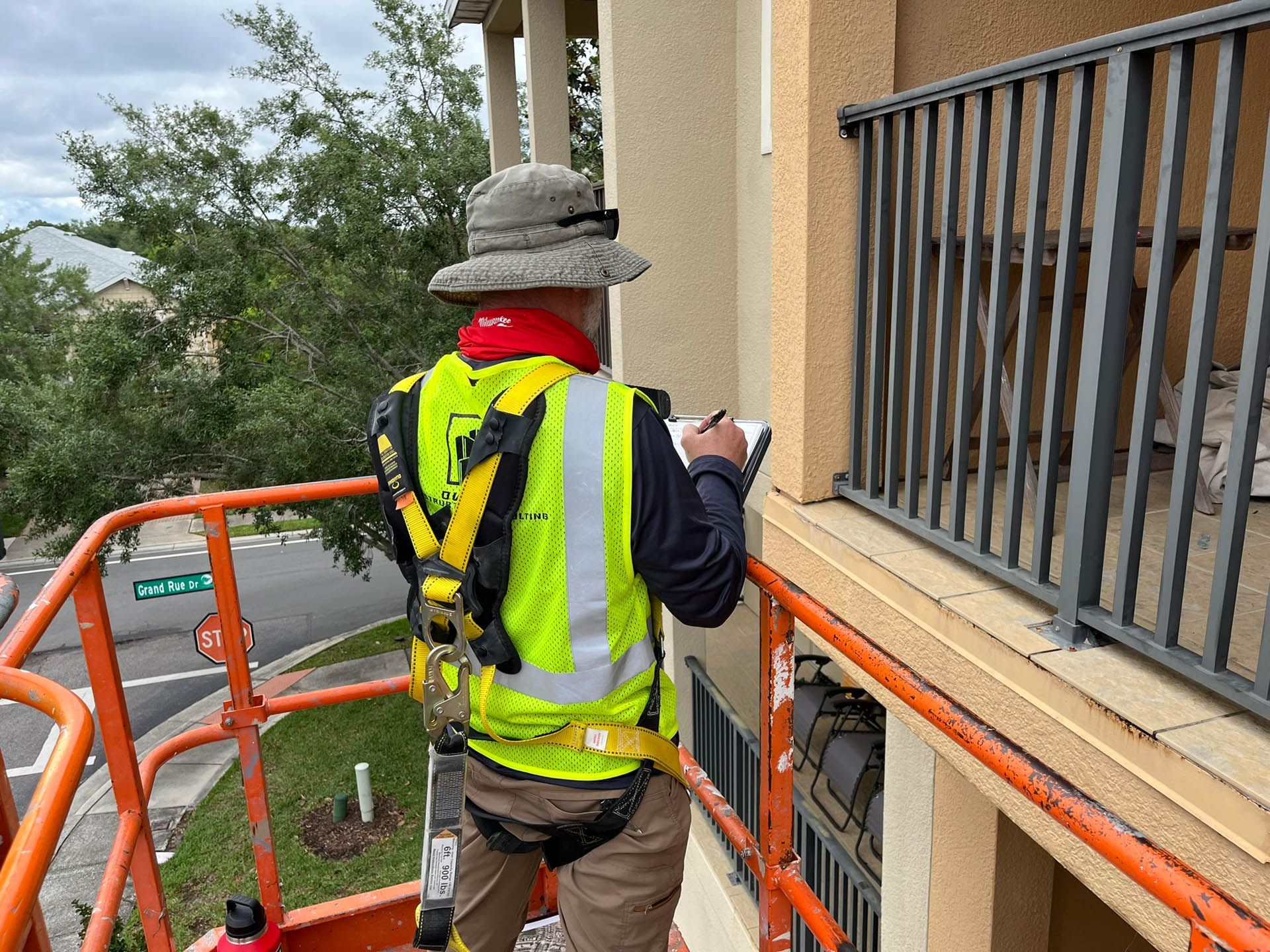 A man is standing on a crane taking notes on a clipboard.