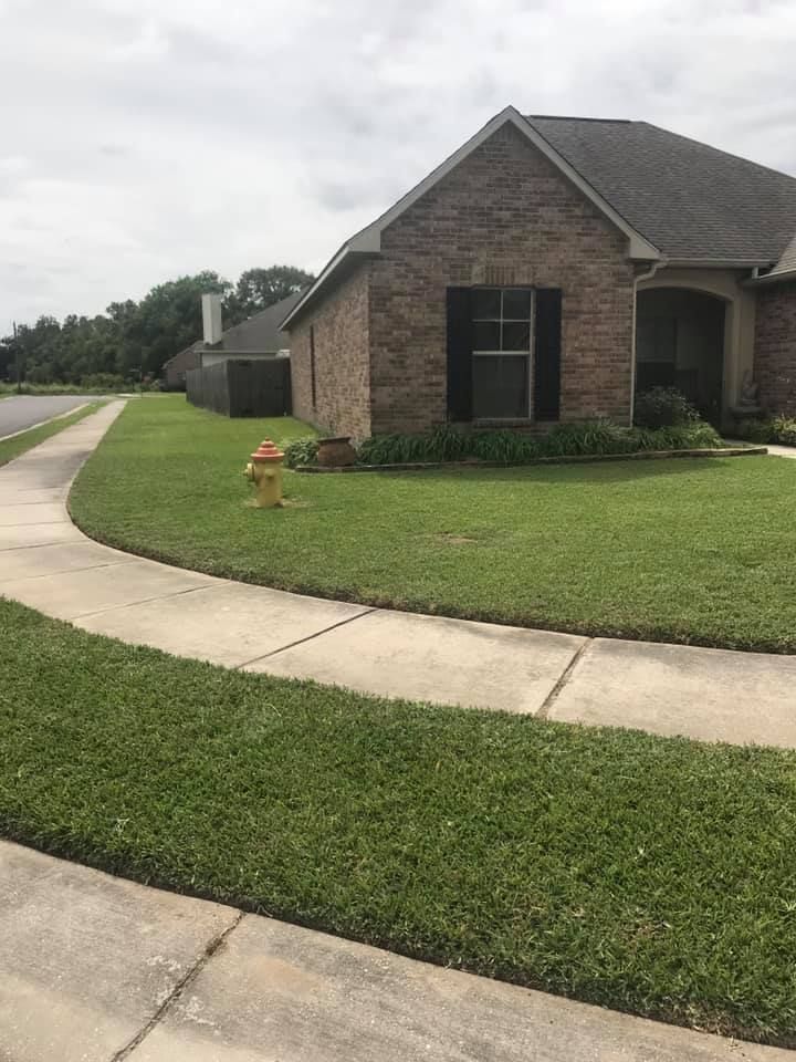 A brick house with black shutters sits on a grassy corner lot next to a sidewalk and a yellow fire hydrant.