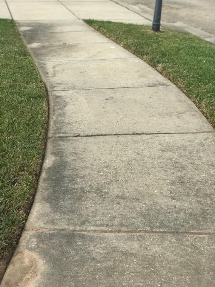 A curved concrete sidewalk flanked by green grass on both sides, viewed from a slightly elevated angle.