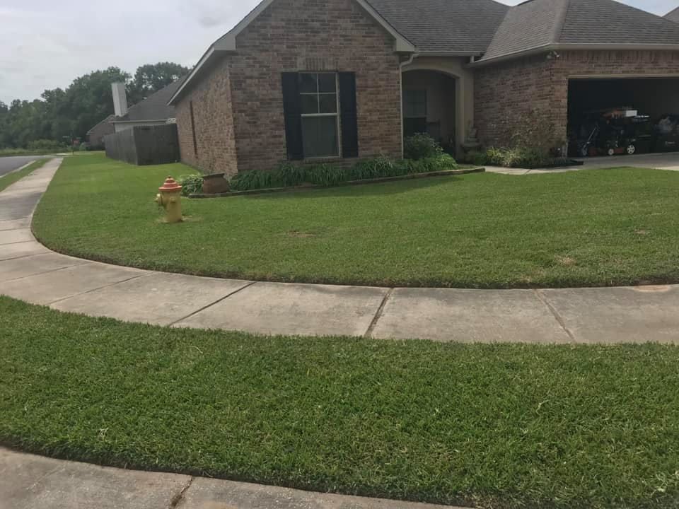 A brick house with a dark garage sits behind a manicured green lawn and a curved concrete sidewalk with a fire hydrant.