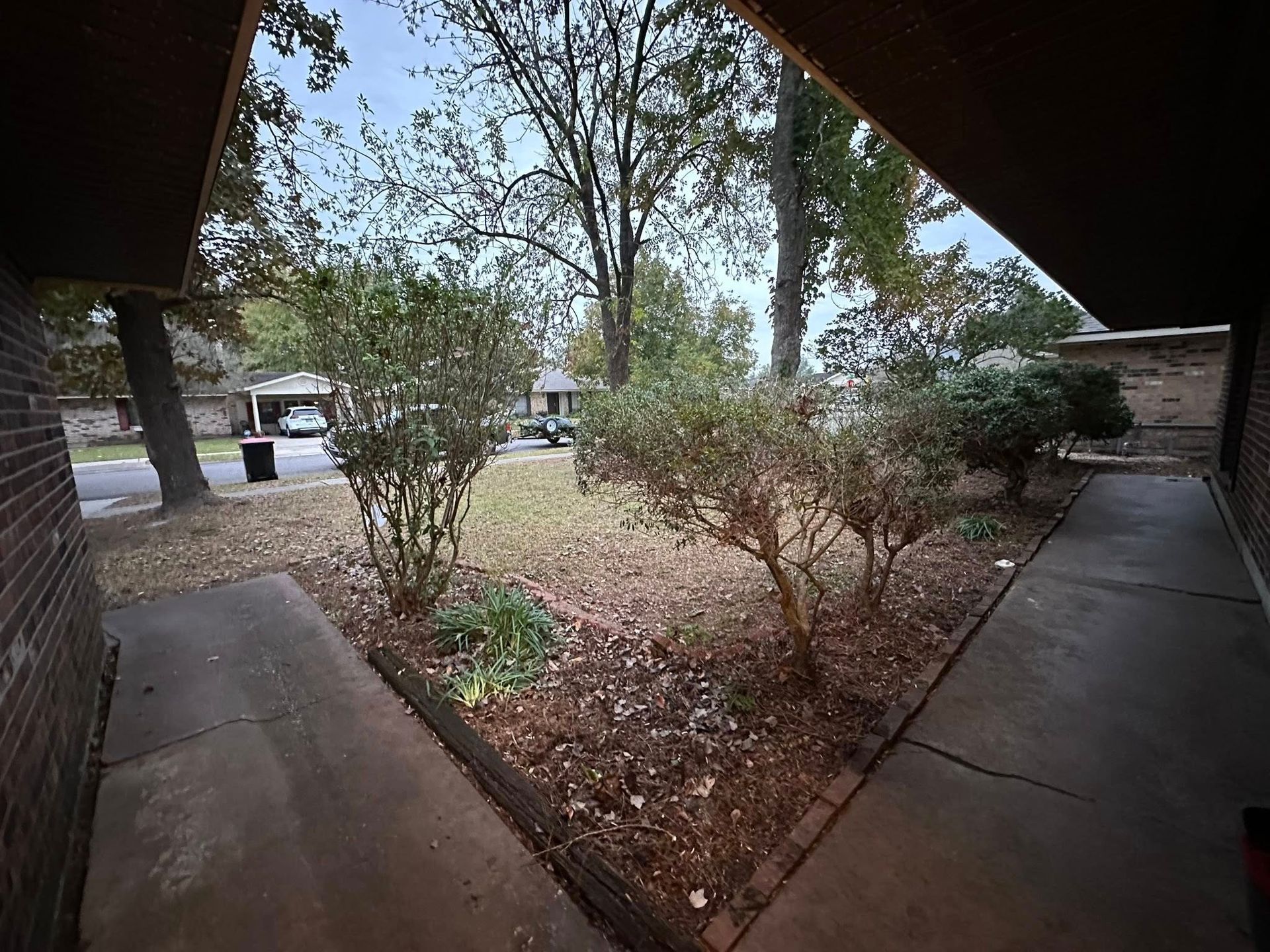A concrete walkway leads to an entry framed by brick walls, overlooking a small yard with bushes and fallen leaves.