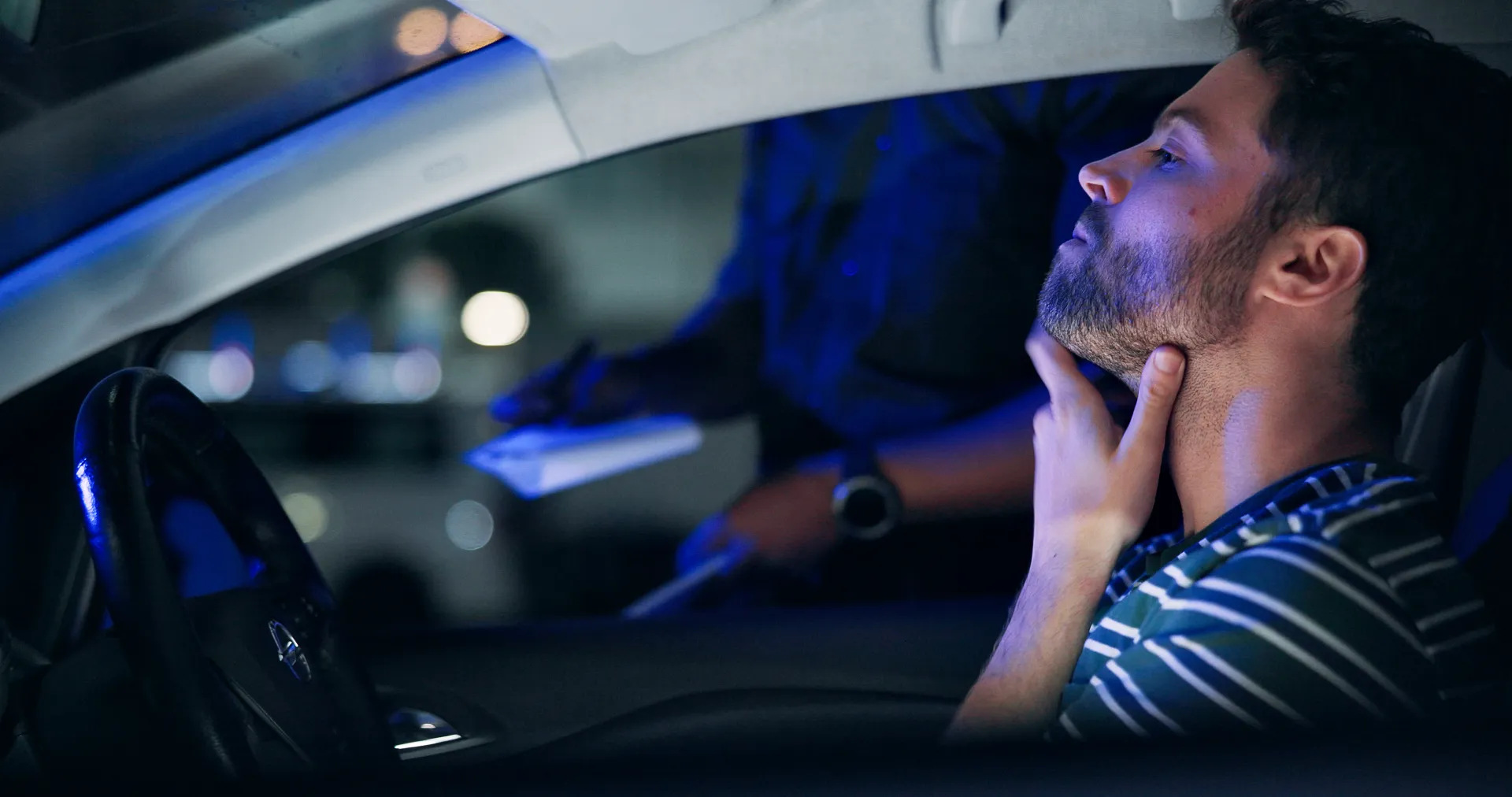 Man in car being questioned by police officer at night.