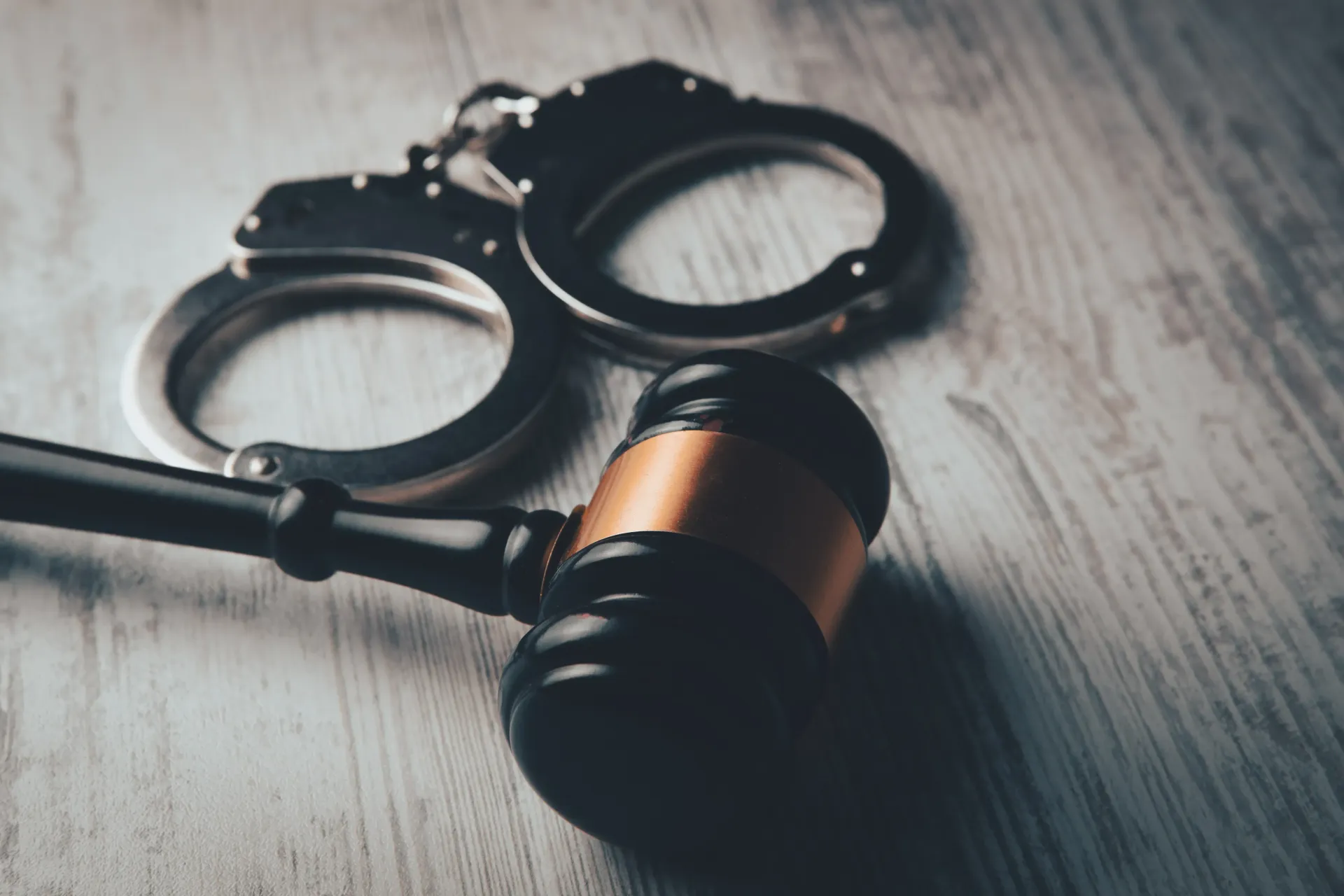 Handcuffs and a judge's gavel on a wooden surface, symbols of law and justice.