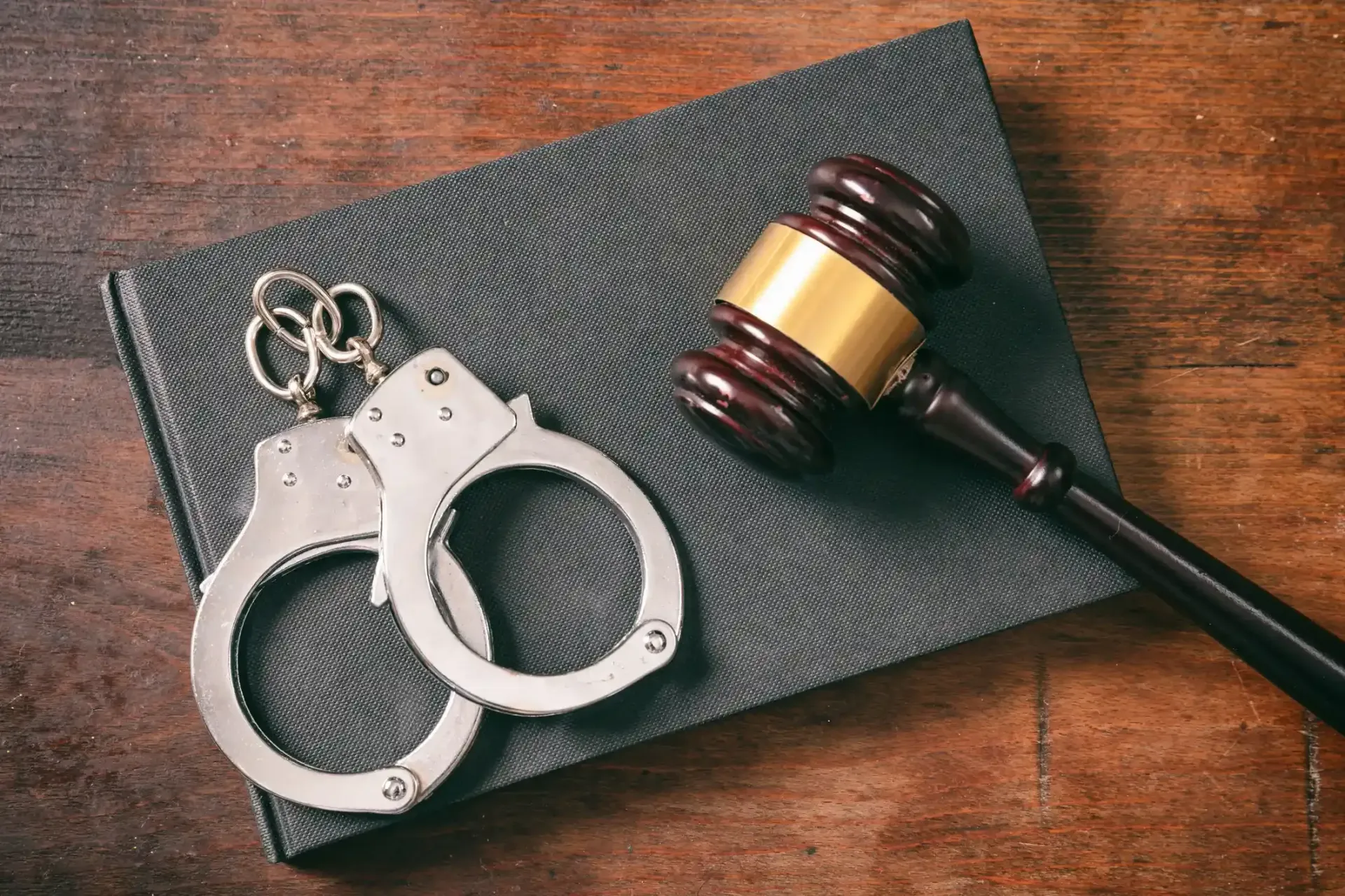 Handcuffs and gavel on a law book on a wooden table.