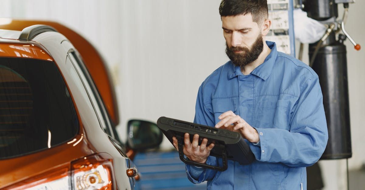 A man is using a tablet in front of a car in a garage.  | Alpha Autoworks