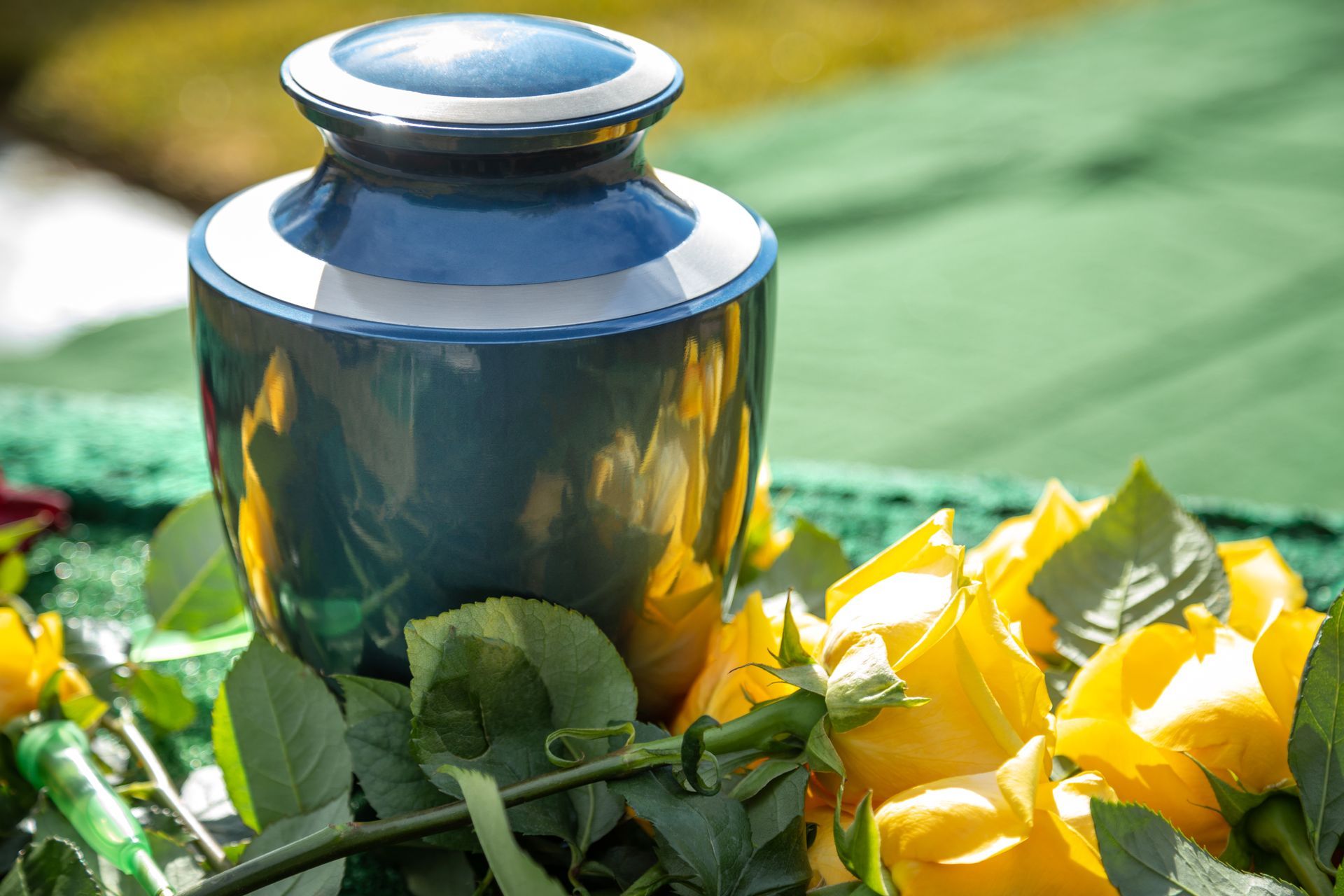Blue and white cremation urn with yellow roses on green cloth.