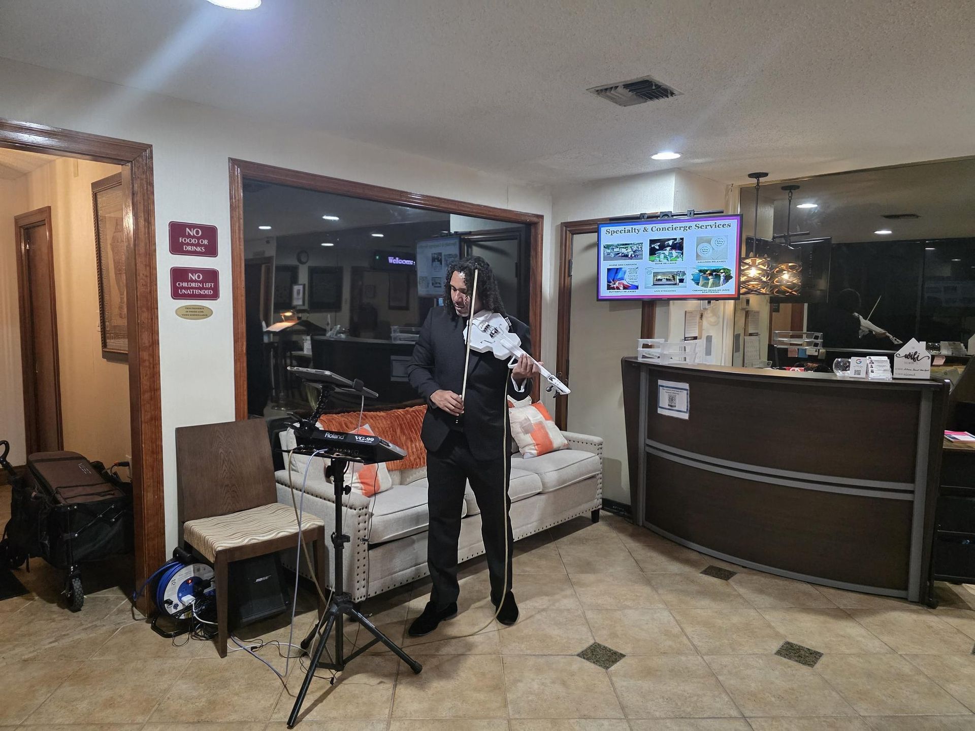 Man playing a white violin in a hotel lobby; he is standing in front of a sofa.