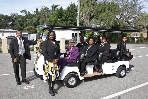 People in formal attire pose near a white golf cart in an outdoor setting.