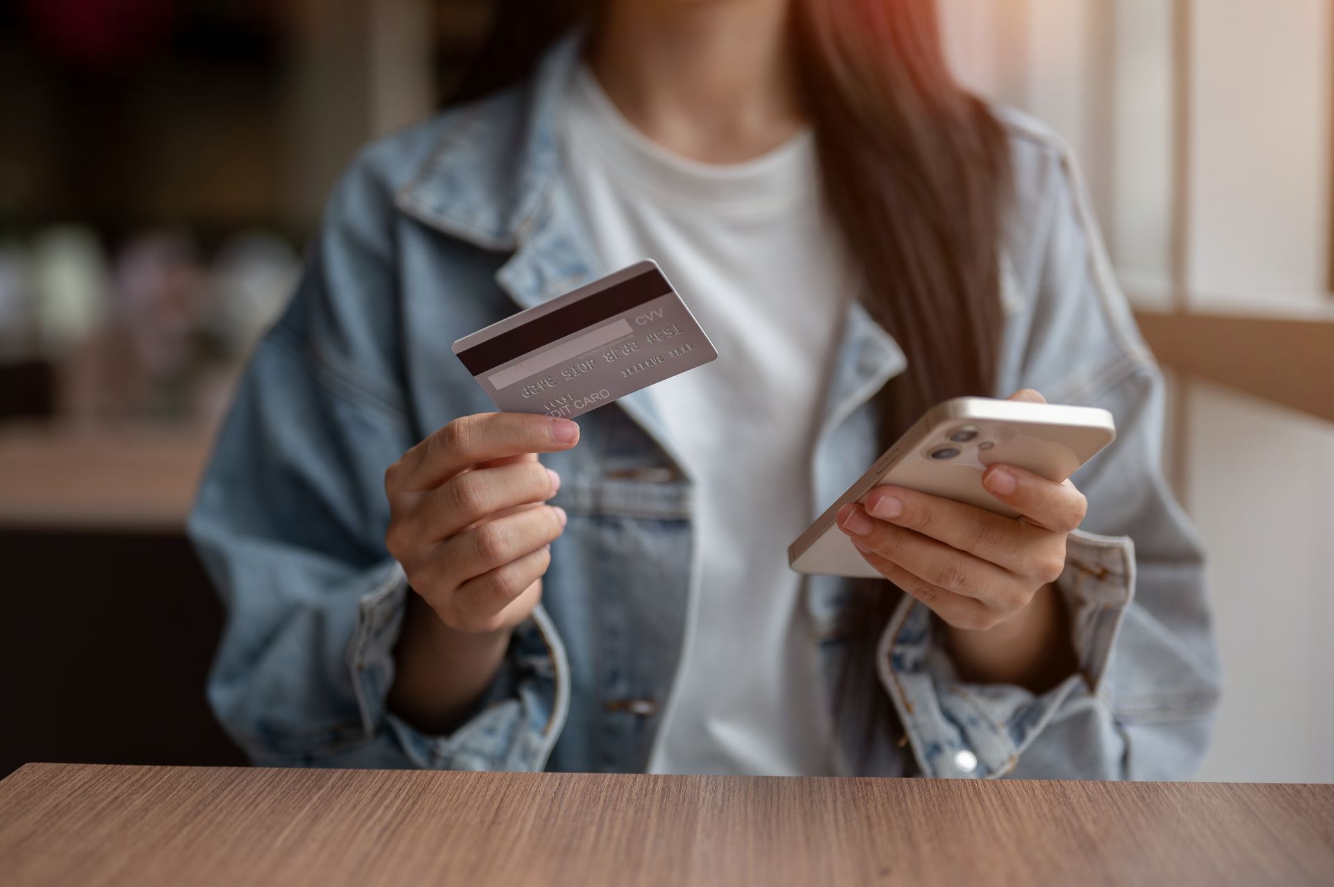 Woman holding a credit card and smartphone, possibly making an online payment.